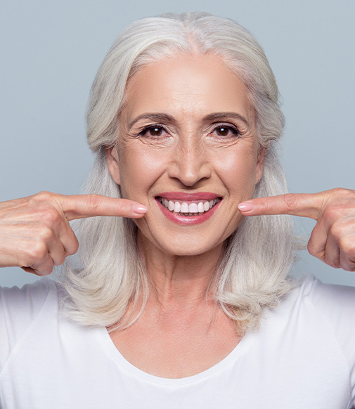 senior woman pointing to her bright, white smile