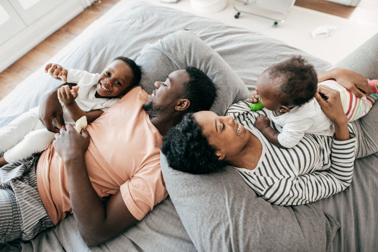 Aerial view of a mom, dad, and two young children smiling on a bed together before visiting their family dentist in Prosper, TX