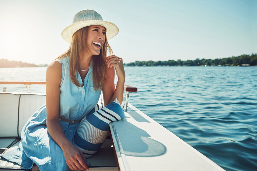 Brunette woman with a beautiful smile after cosmetic dentistry relaxes on a boat in the water