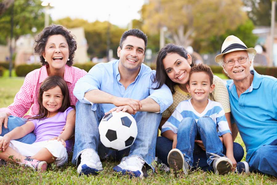 Multigenerational hispanic family sitting on the grass with a soccer ball.