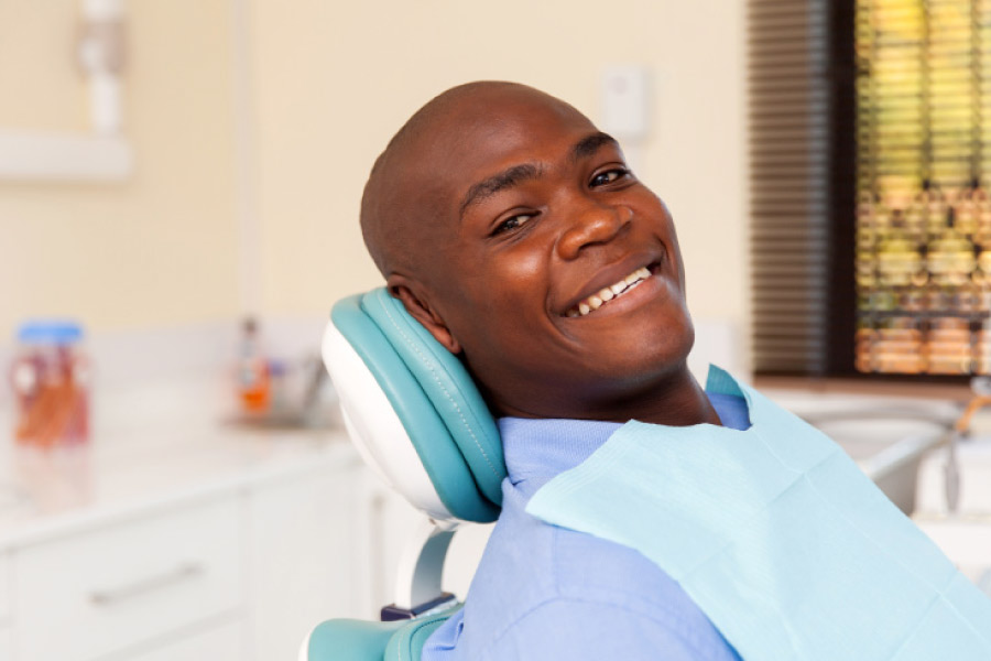Smiling black man in the dental chair for a preventive hygiene cleaning and exam.